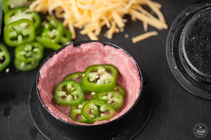 a raw burger patty with sliced jalapenos inside