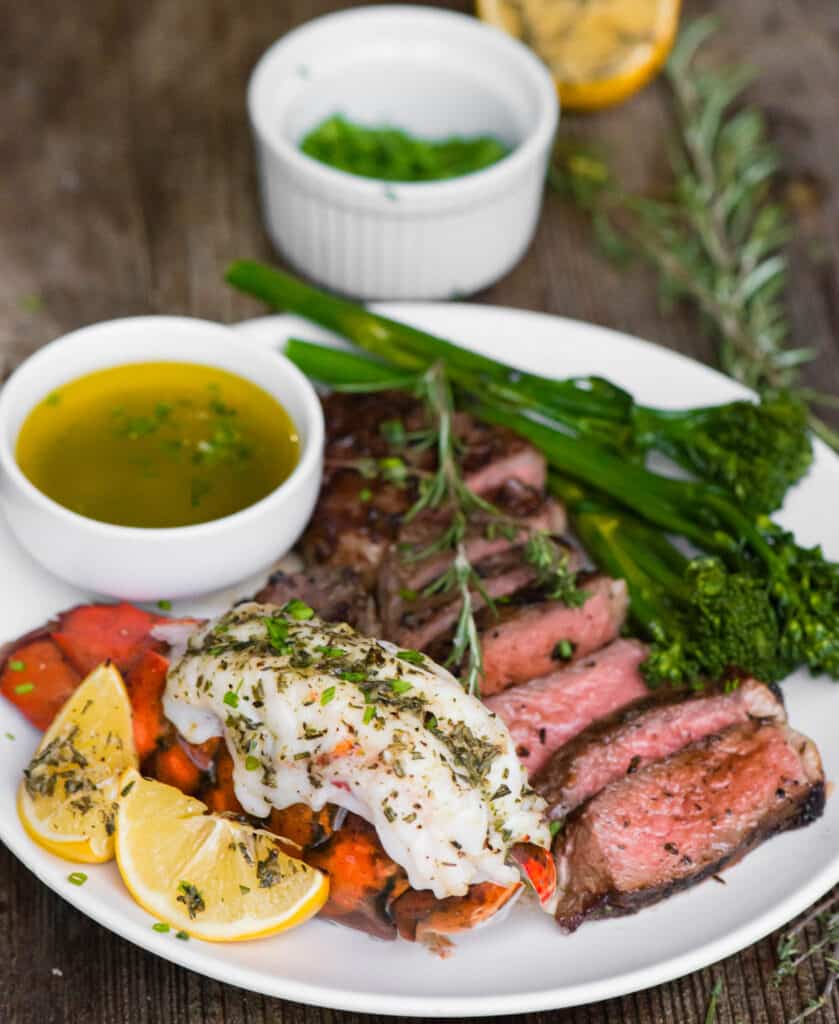 broiled lobster and sliced steak on plate with melted butter and broccolini.