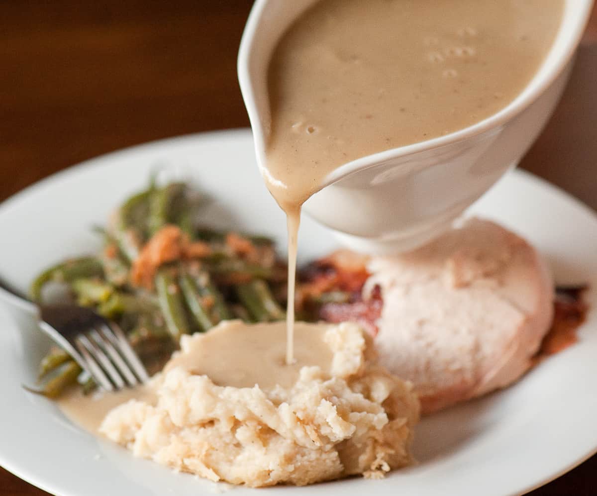 pouring homemade turkey giblet gravy over mashed potatoes.