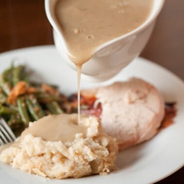 pouring homemade turkey giblet gravy over mashed potatoes.