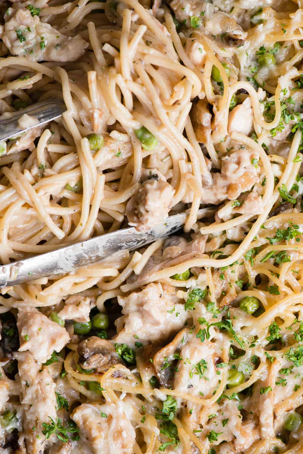 tongs holding spaghetti with turkey, vegetables, and cream sauce
