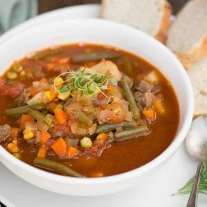 white bowl with vegetable beef soup and bread on the side