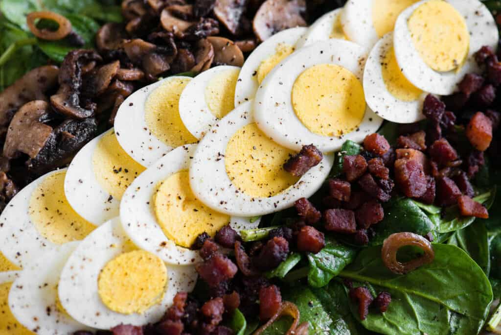 slices of hard boiled egg with cooked bacon on spinach salad