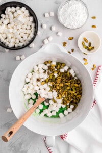 Adding mini marshmallows and pistachios to crushed pineapple and pistachio pudding mix.